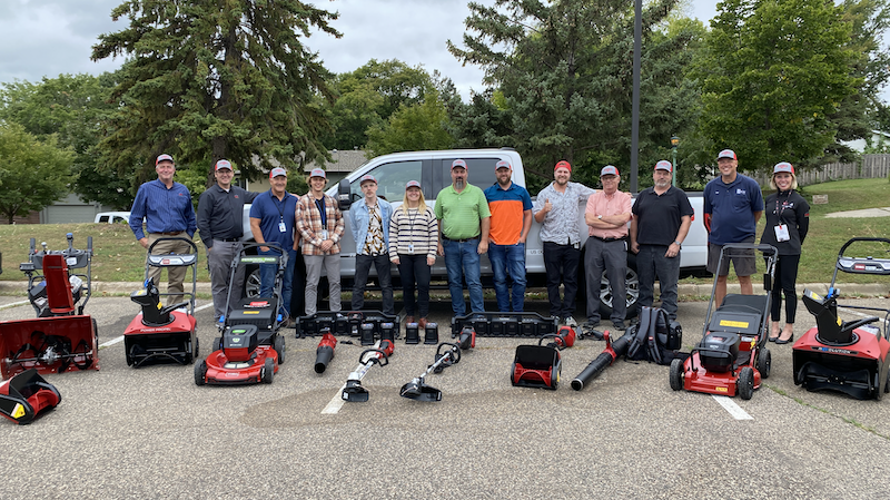 Group of people standing behind Toro electric lawn and snow equipment